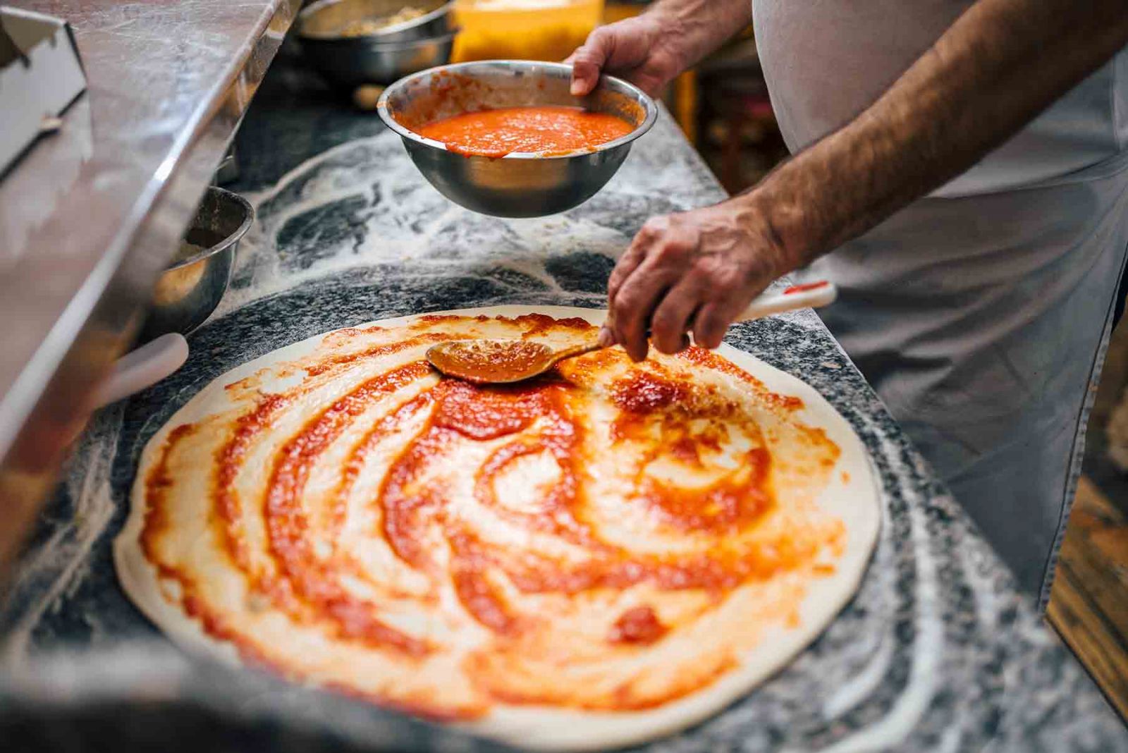 Chef spreading sauce on a pizza crust