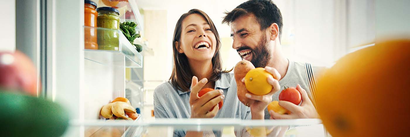 Couple opening their fridge and smiling because it's stocked with food