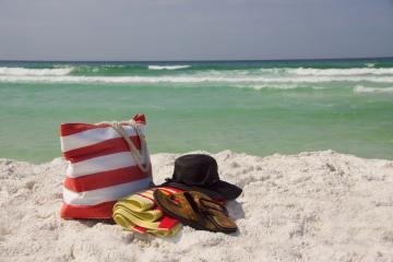 beach bag, towel, flip flops, and a hat on the shore with view of water in background
