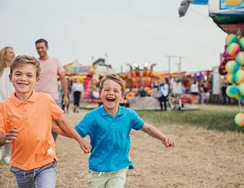 Two young boys running and smiling at a fair