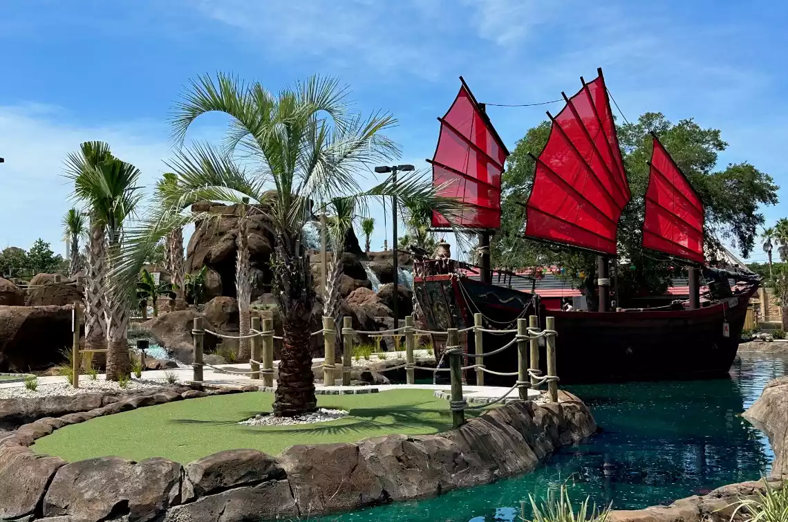 Red Dragon Cove Adventure Golf in Myrtle Beach Asian-themed mini golf course at Red Dragon Cove Adventure Golf featuring a ship with red sails, tropical landscaping, bridges, and water features in Myrtle Beach.