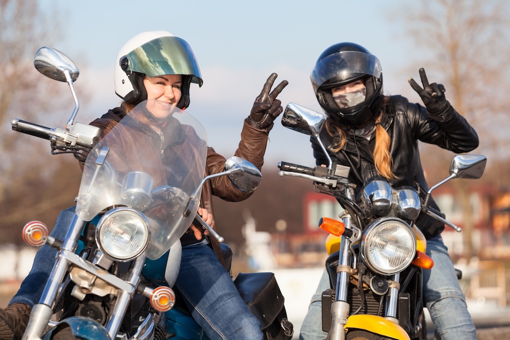 Victory signs in leather gloves from two laughing female bikers with street motorcycles.