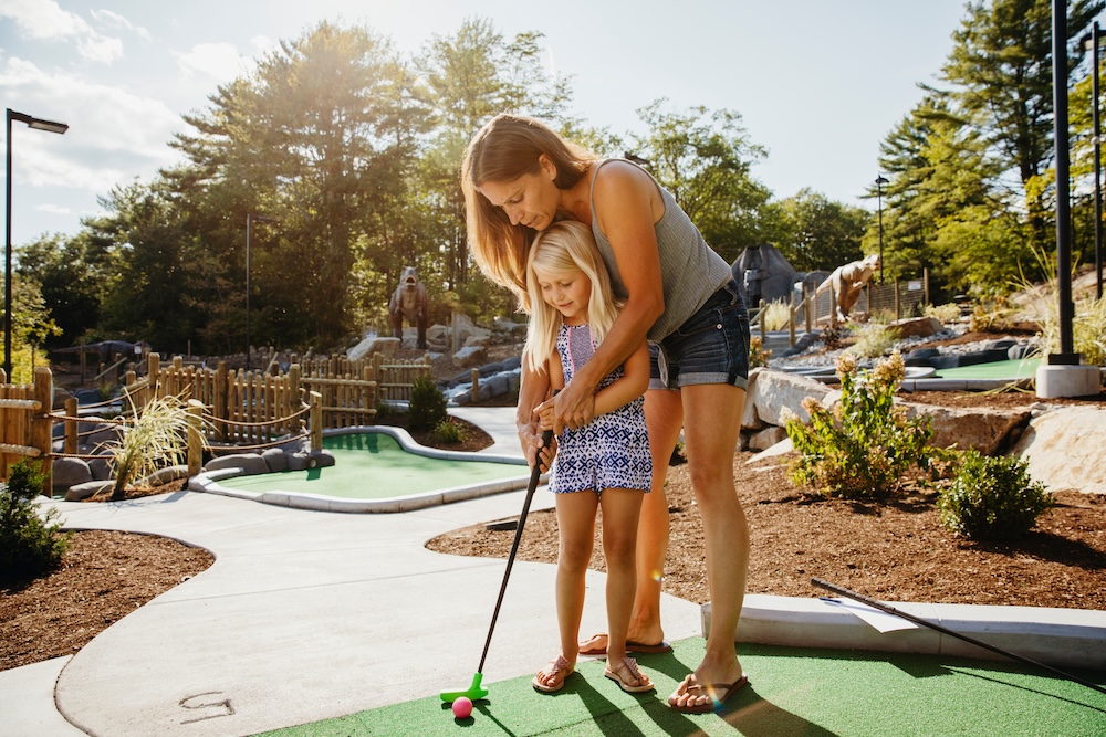 Woman teaching daughter to play golf at miniature golf course